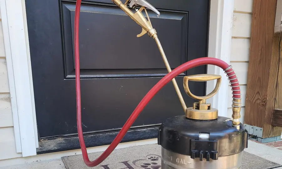 A Rozier Pest Control & Waterproofing technician treating a residential porch with a professional sprayer.