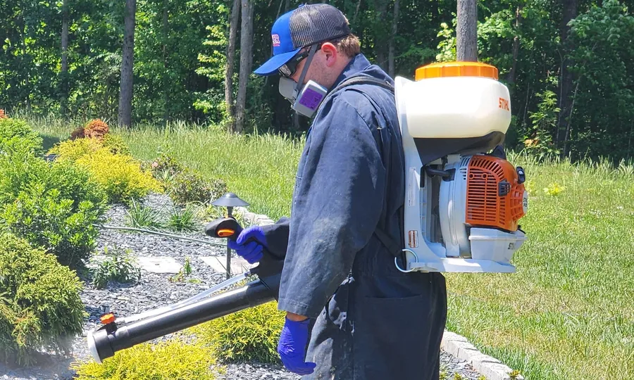A Rozier Pest Control & Waterproofing technician applying an outdoor mosquito misting treatment with a backpack sprayer.