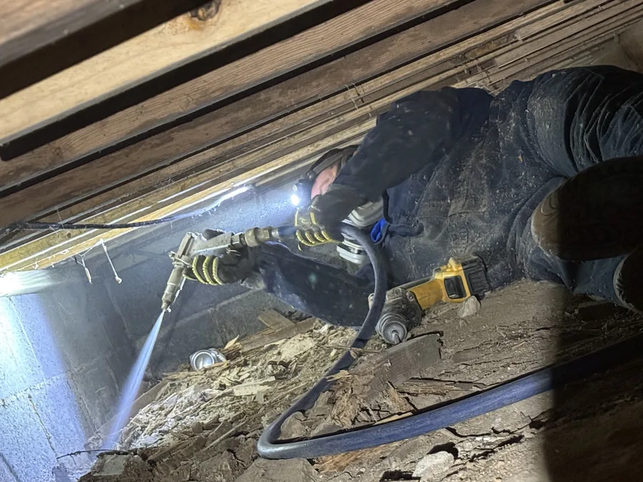 A Rozier Pest Control & Waterproofing technician applying a borate wood treatment to crawl space joists with a spray gun.